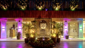 A hotel lobby with a central decorative wall, potted plants, and a fountain. - Gold The Royal (New Delhi)