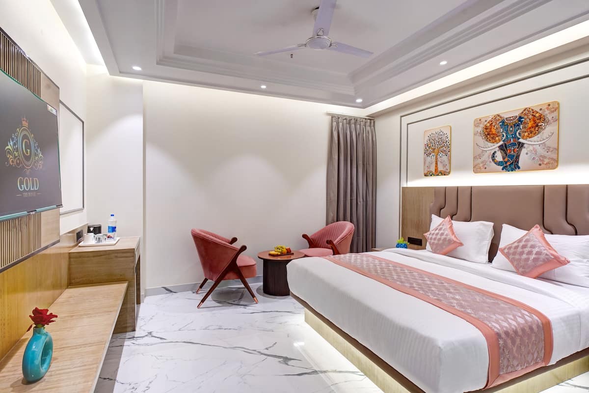 Quarto de hotel com uma cama grande, televisão, pequena mesa com um vaso e duas cadeiras.
