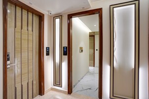 Un couloir avec une porte en bois et un mur recouvert de miroirs, qui mène à une salle de bain.