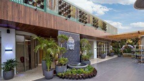 A modern building with a wooden facade, a large Buddha statue, and potted plants arranged in a circular pattern. - Gold The Royal (New Delhi)