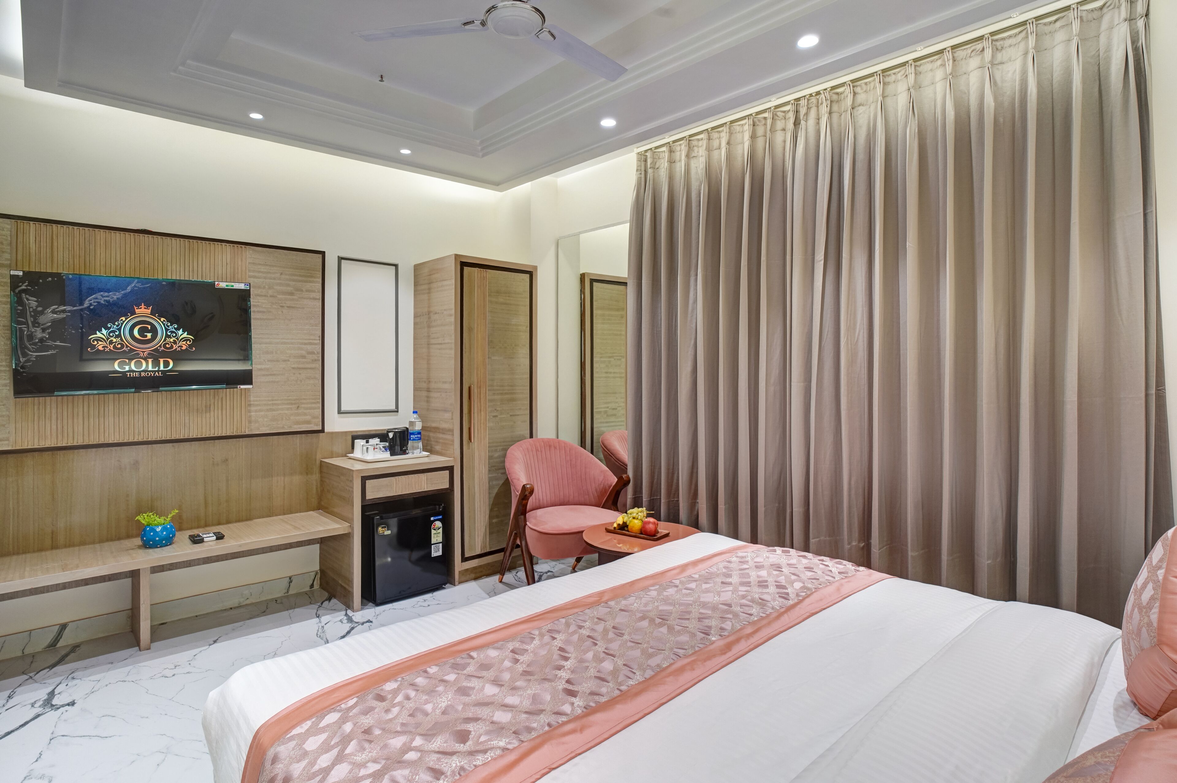 A hotel room with a bed, a desk with a computer, a chair, a TV, and a large window with curtains.