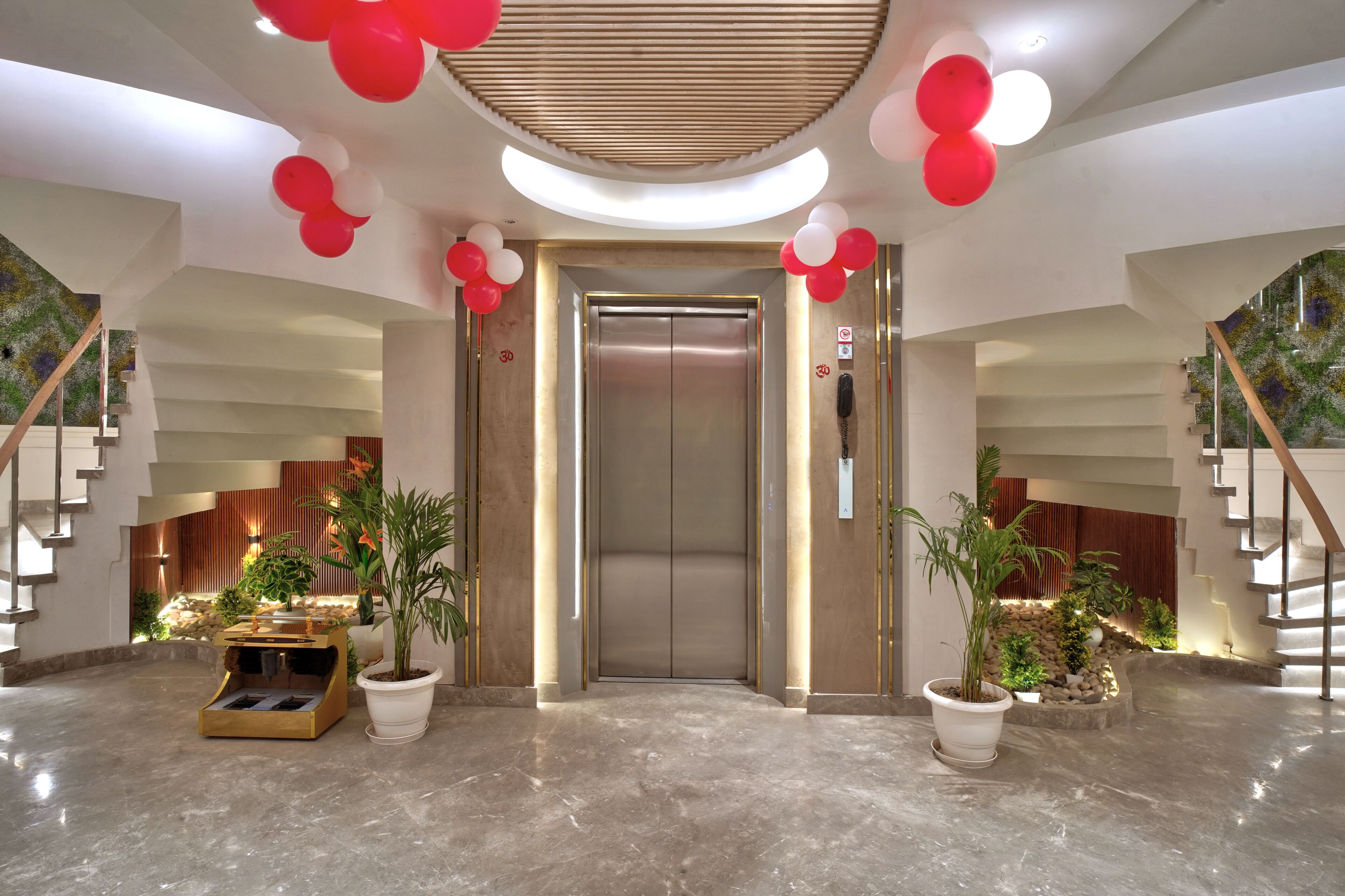 A modern lobby with a central elevator, potted plants, and a marble floor.