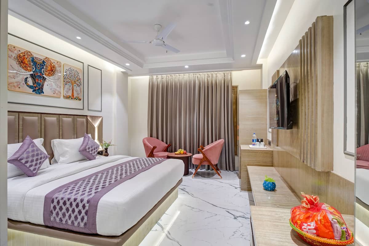Quarto de hotel moderno com uma cama grande, duas cadeiras cor-de-rosa, uma mesinha com frutas, televisão e obras de arte na parede.