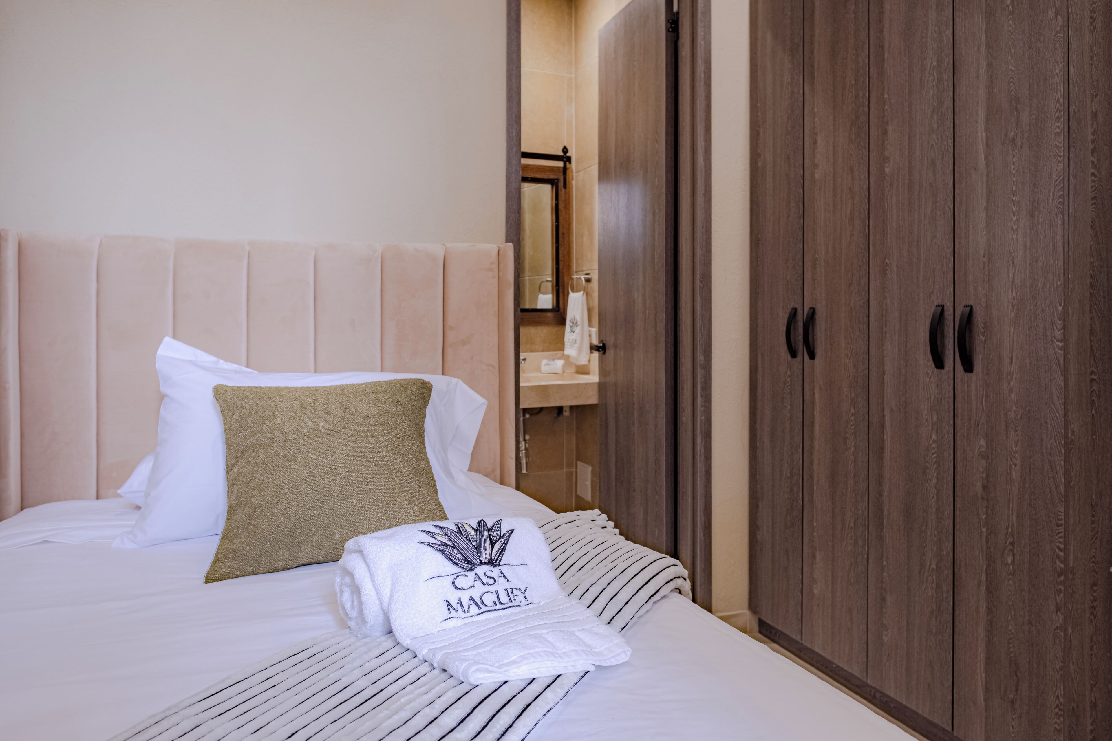 A hotel room with a bed, a wooden wardrobe, and a bathroom visible through an open door.