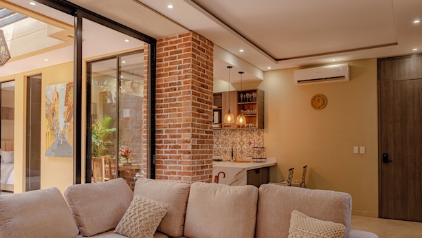 Una sala moderna con un sofá color crema, una pared decorada con ladrillo y una puerta de cristal que da a un balcón.