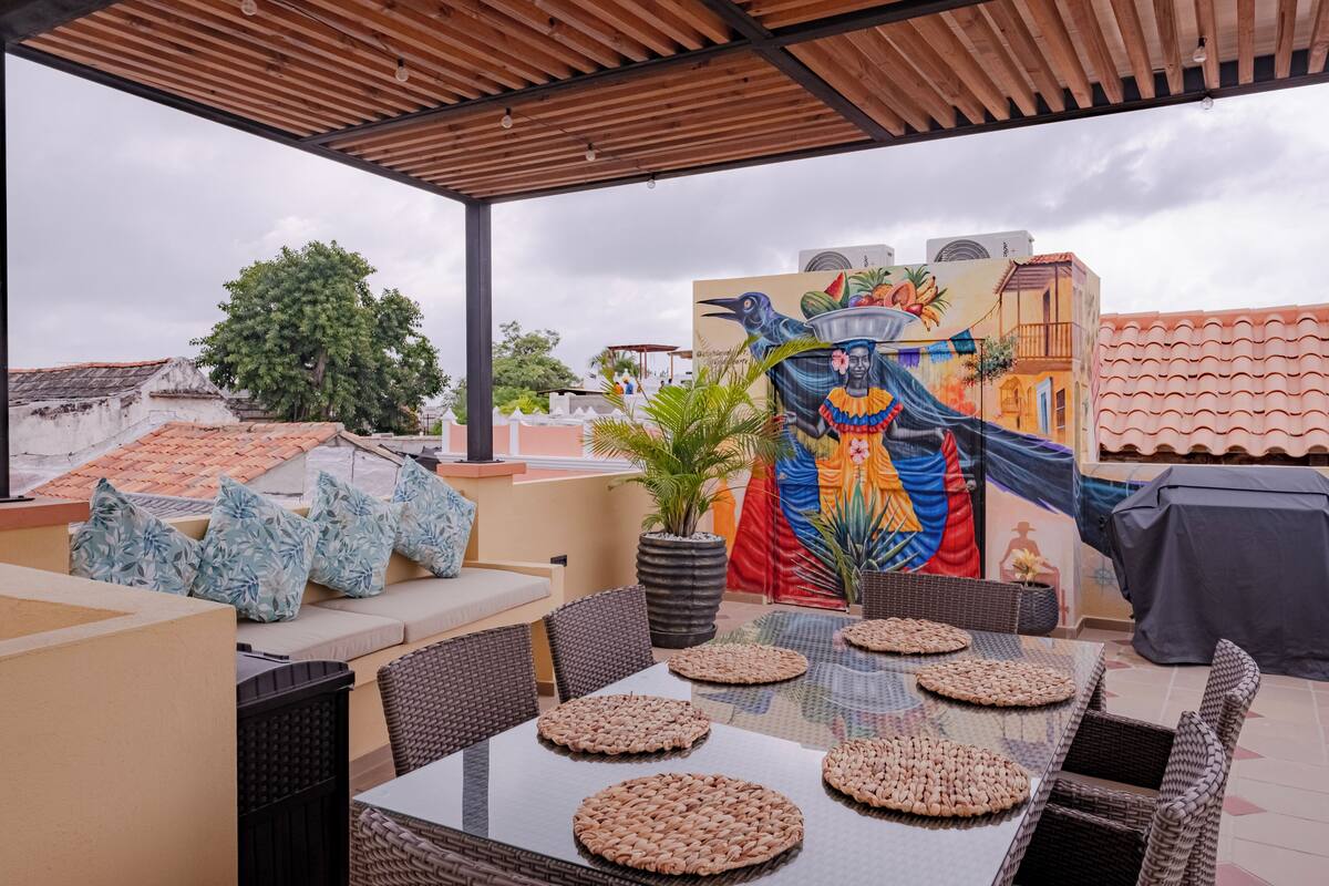 An outdoor patio with a dining table, wicker chairs, and a mural on the wall.