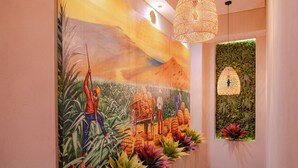 Un mural con motivos agrícolas, una lámpara colgante de tejido y una pared verde con plantas.