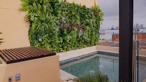 Un área de piscina con un muro verde exuberante, una terraza de madera y vistas al horizonte de la ciudad.