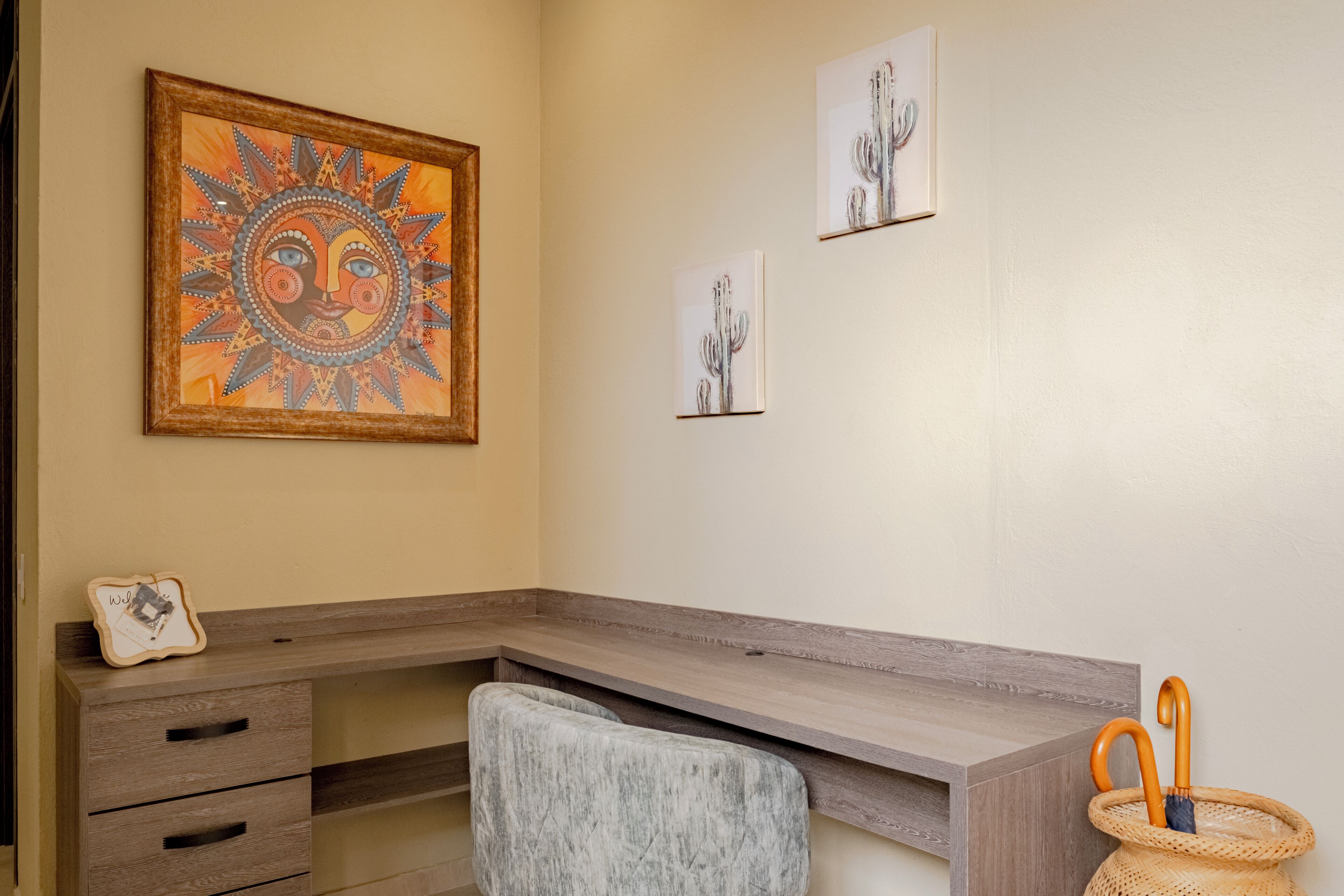A room with a wooden desk, a cushioned chair, and a framed artwork on the wall.