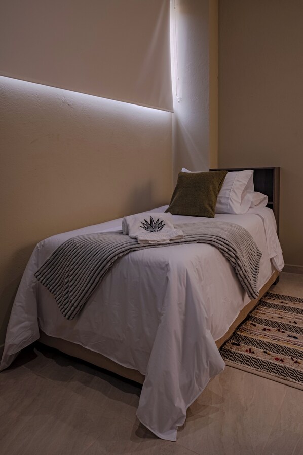 Una cama bien hecha con sábanas blancas, almohada marrón y una manta decorativa.
