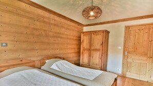 A wooden-paneled room with two beds, a wardrobe, and a hanging light fixture.