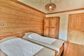 Um quarto com painéis de madeira, duas camas, um guarda-roupa e um lustre.
