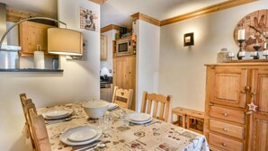 A dining area with a table set for four, wooden cabinets, a wall clock, and a shelf with kitchen items.