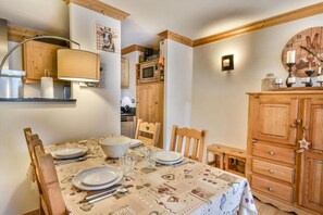 Uma sala de jantar com uma mesa posta para quatro pessoas, armários de madeira, um relógio de parede e uma prateleira com utensílios de cozinha.