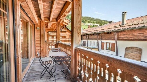 A wooden balcony with a table and chairs, overlooking a mountainous landscape.