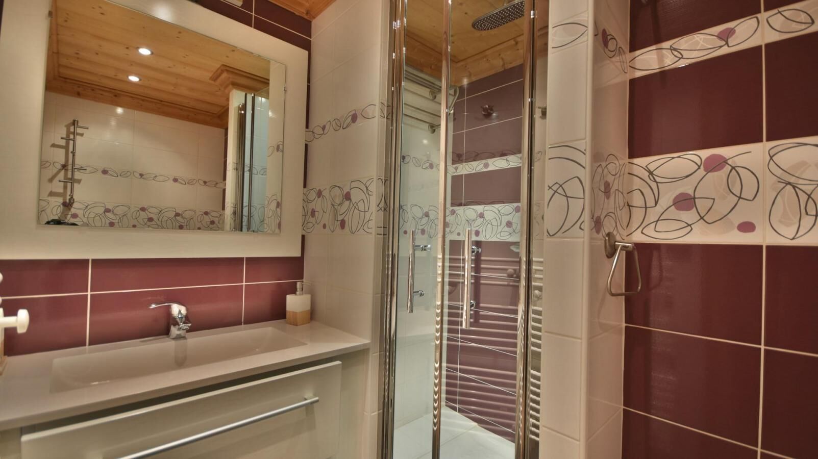 Une salle de bain avec une douche à parois de verre, un lavabo avec un miroir au-dessus et des carreaux décoratifs.