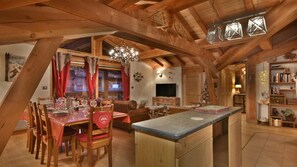 Um amplo loft com área de jantar, cozinha e sala de estar, com vigas de madeira aparentes e um ambiente acolhedor.