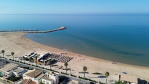 Una zona costera con playa de arena, un muelle que se adentra en el agua y edificios a lo largo del paseo marítimo.