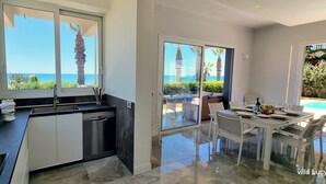 Una cocina moderna con vista al mar, un comedor con mesa de vidrio y vistas a la piscina.