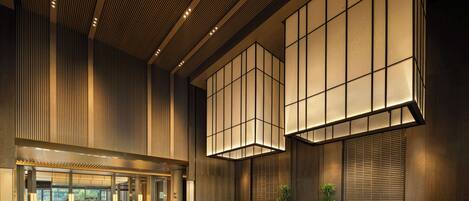 A spacious lobby with a modern design, featuring a reception desk, seating area, and large windows.