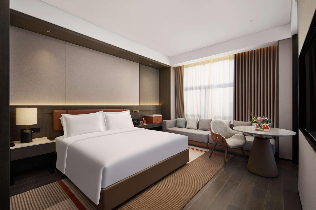 Ein modernes Hotelzimmer mit einem großen Bett, einer Couch, einem Esstisch und Blick auf die Stadt.