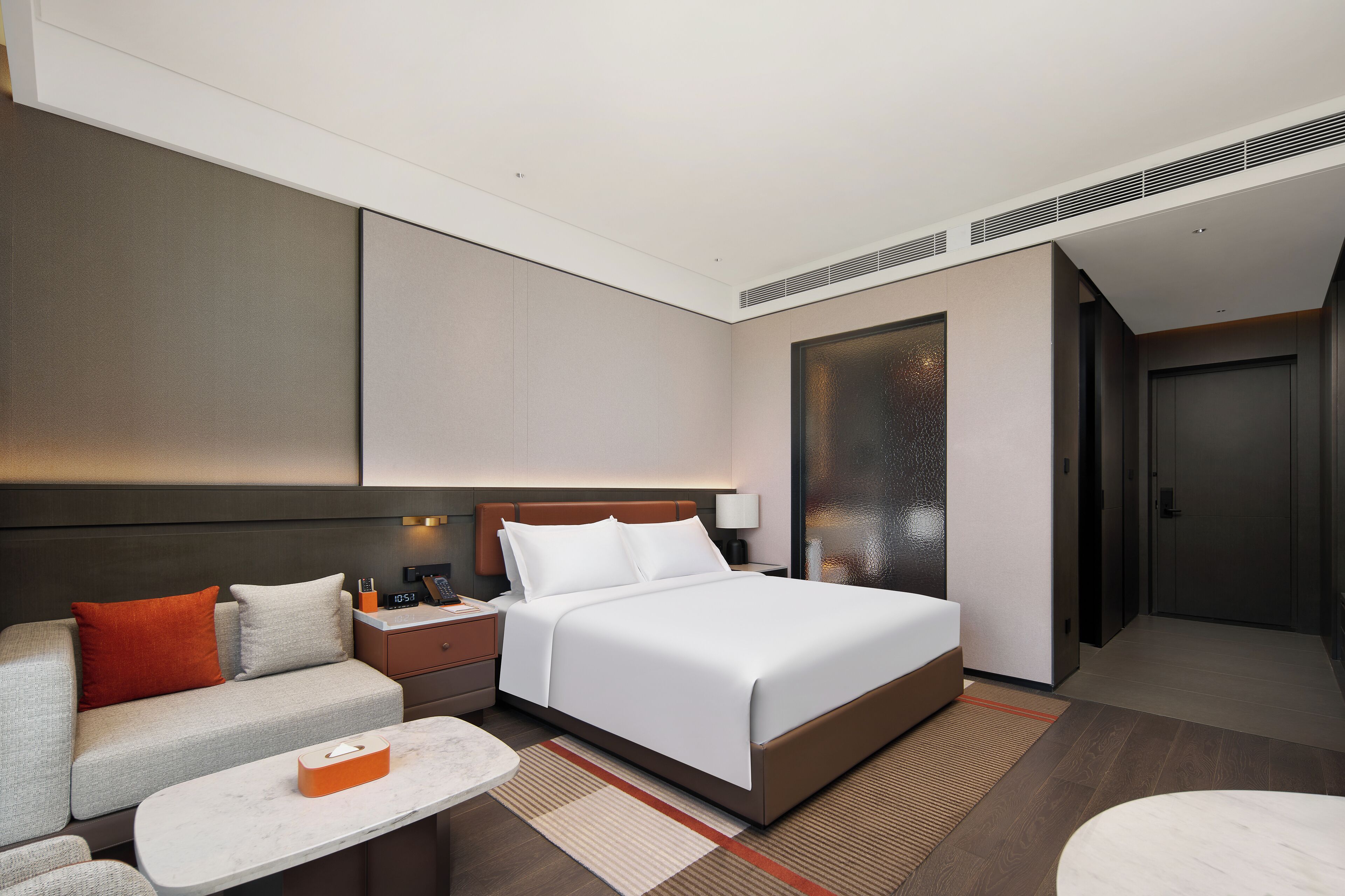 Una habitación de hotel moderna con una cama grande, un sofá, una pequeña mesa y una mesita de noche.