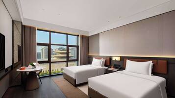 A hotel room with two beds, a desk, and a large window offering a city view.