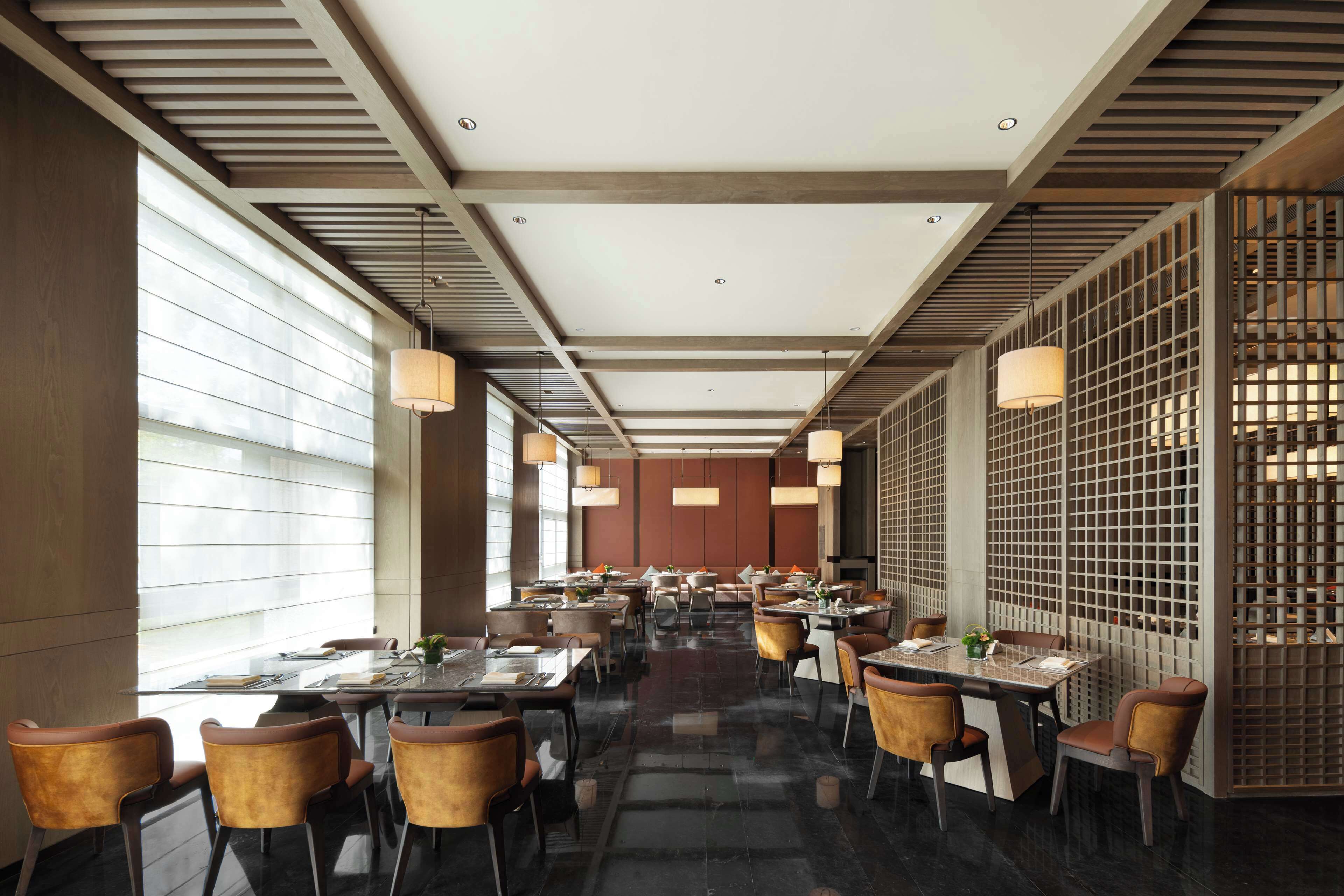 A modern dining area with tables and chairs, large windows, and a decorative partition.