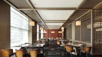 A modern dining area with tables and chairs, large windows, and a decorative partition.