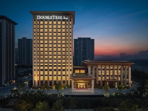A high-rise hotel with a prominent "DOUBLETREE by Hilton" sign, surrounded by other buildings and a landscaped area with trees and pathways. - Doubletree By Hilton Kaifeng (Kaifeng)