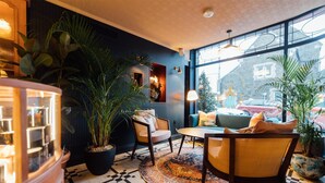 A cozy room with a checkered floor, a round coffee table, and two chairs. There are potted plants and a large window with a view of a building outside. - The Marcus Portrush, Tapestry Collection by Hilton (Portrush)