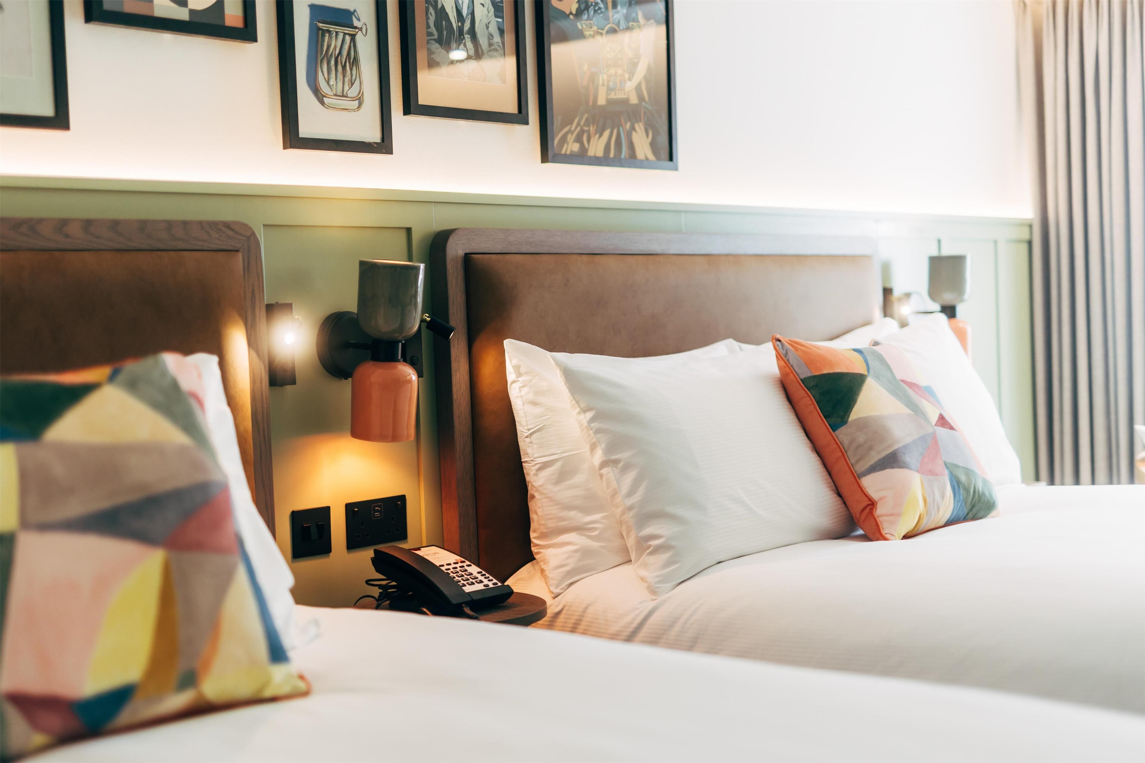 A hotel room with two beds, each with a wooden headboard, a bedside table with a lamp, and a telephone.