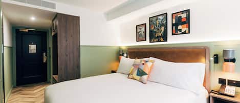 Una habitación de hotel con una cama grande, cabecera de madera, mesita de noche con lámpara y una obra de arte en la pared.