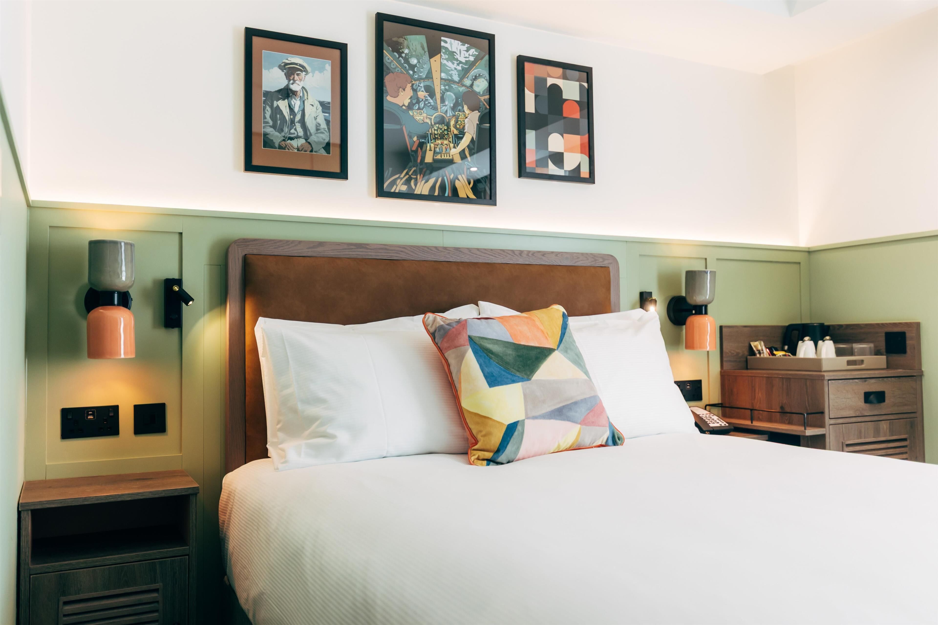 A hotel room with a large bed, two bedside tables, and three framed artworks on the wall.