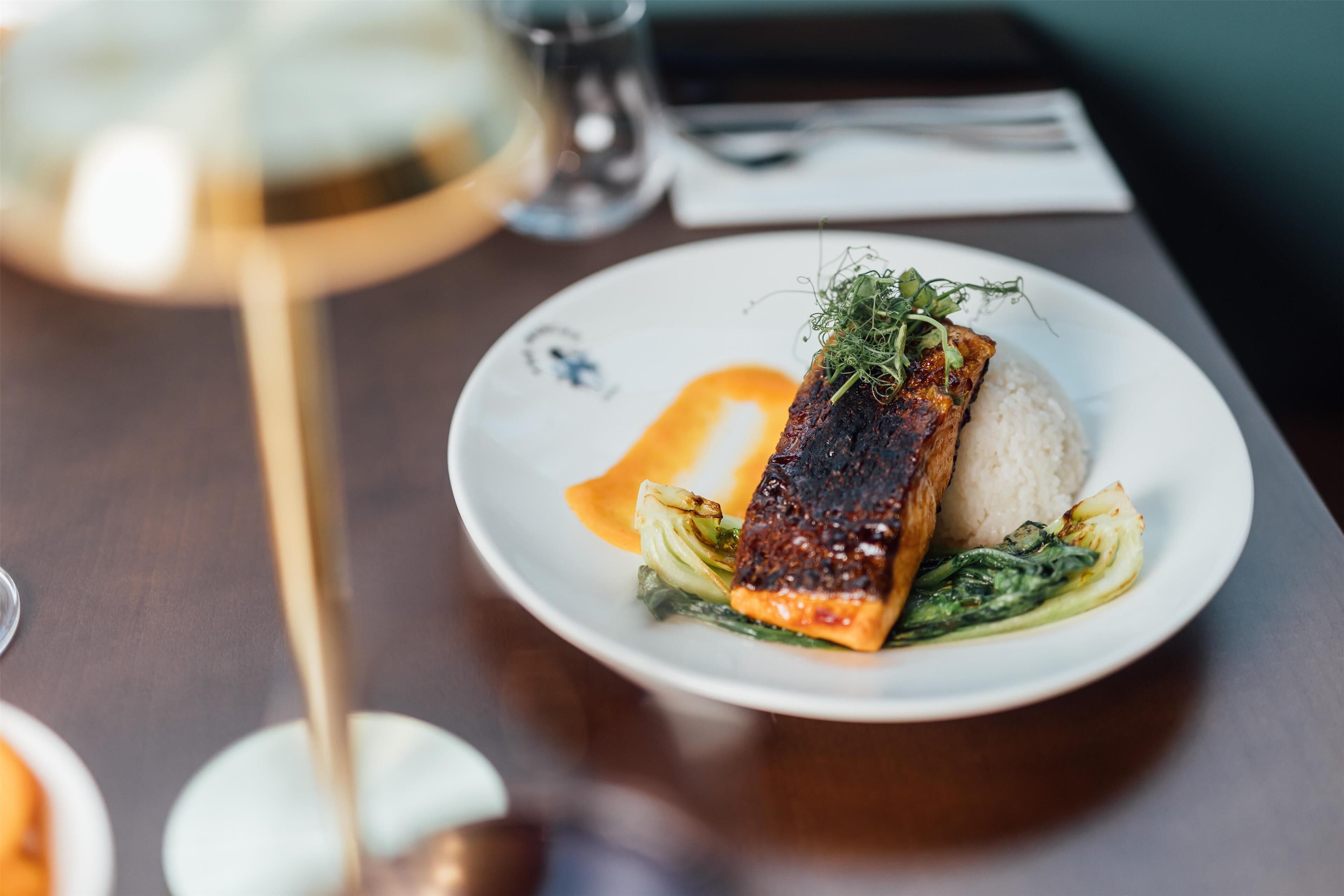 Une assiette de nourriture comprenant du saumon, du riz et des légumes verts, le tout présenté sur une assiette blanche.