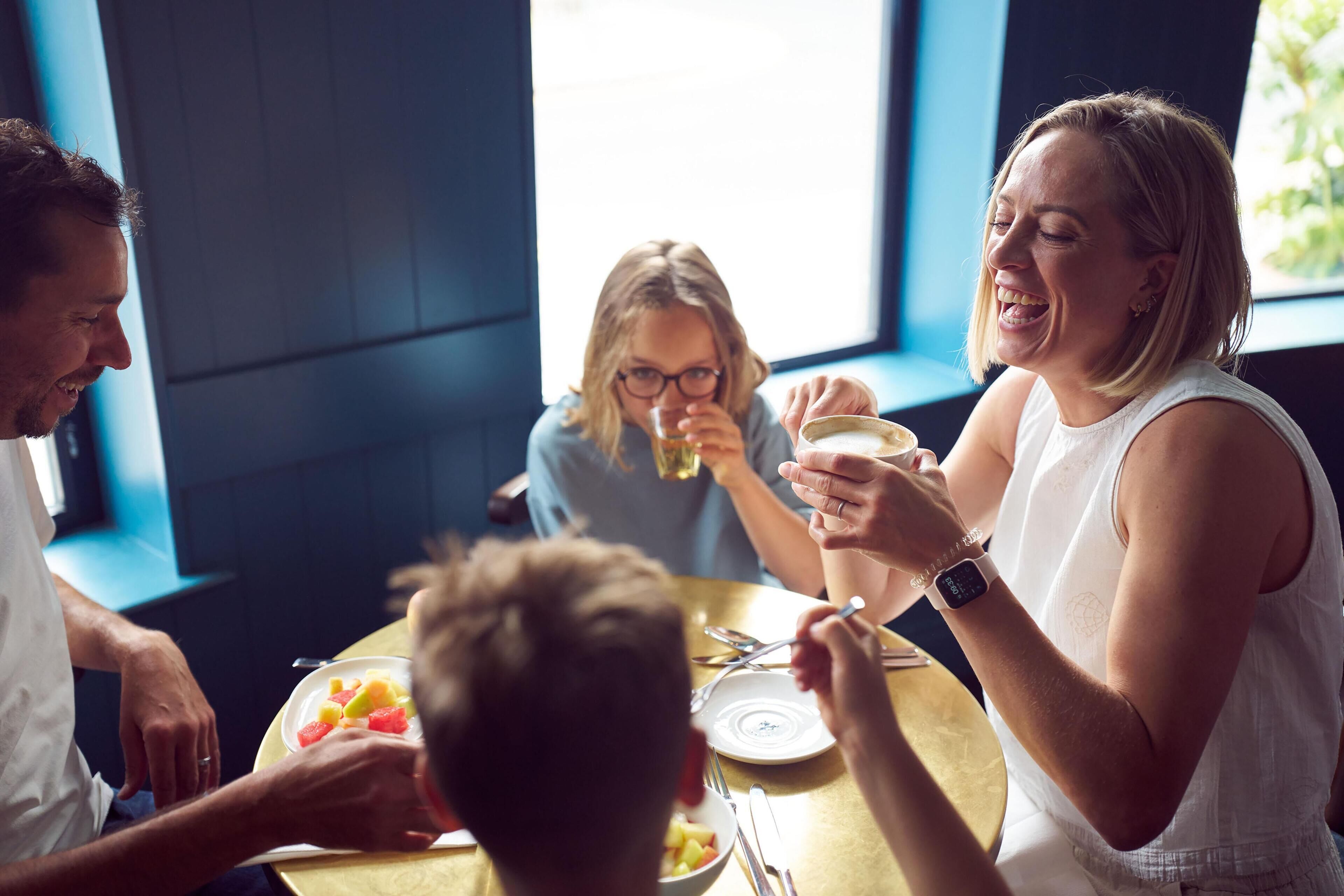 Un grupo de personas cenando en una mesa con diversos platos, incluyendo fruta y una taza de café.