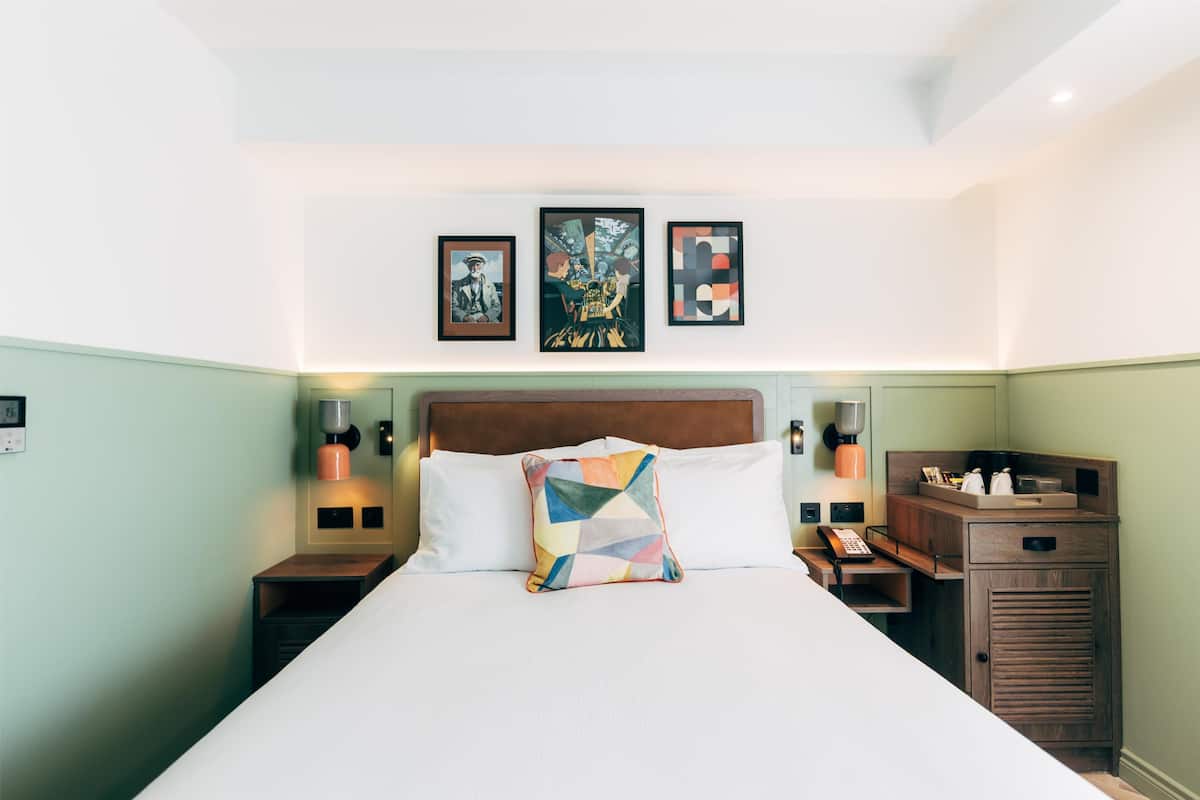 A hotel room with a large bed, a wooden headboard, bedside tables with lamps, and artwork on the wall.