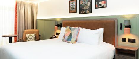 A hotel room with a large bed, a chair, a bedside table, and two wall-mounted lamps.