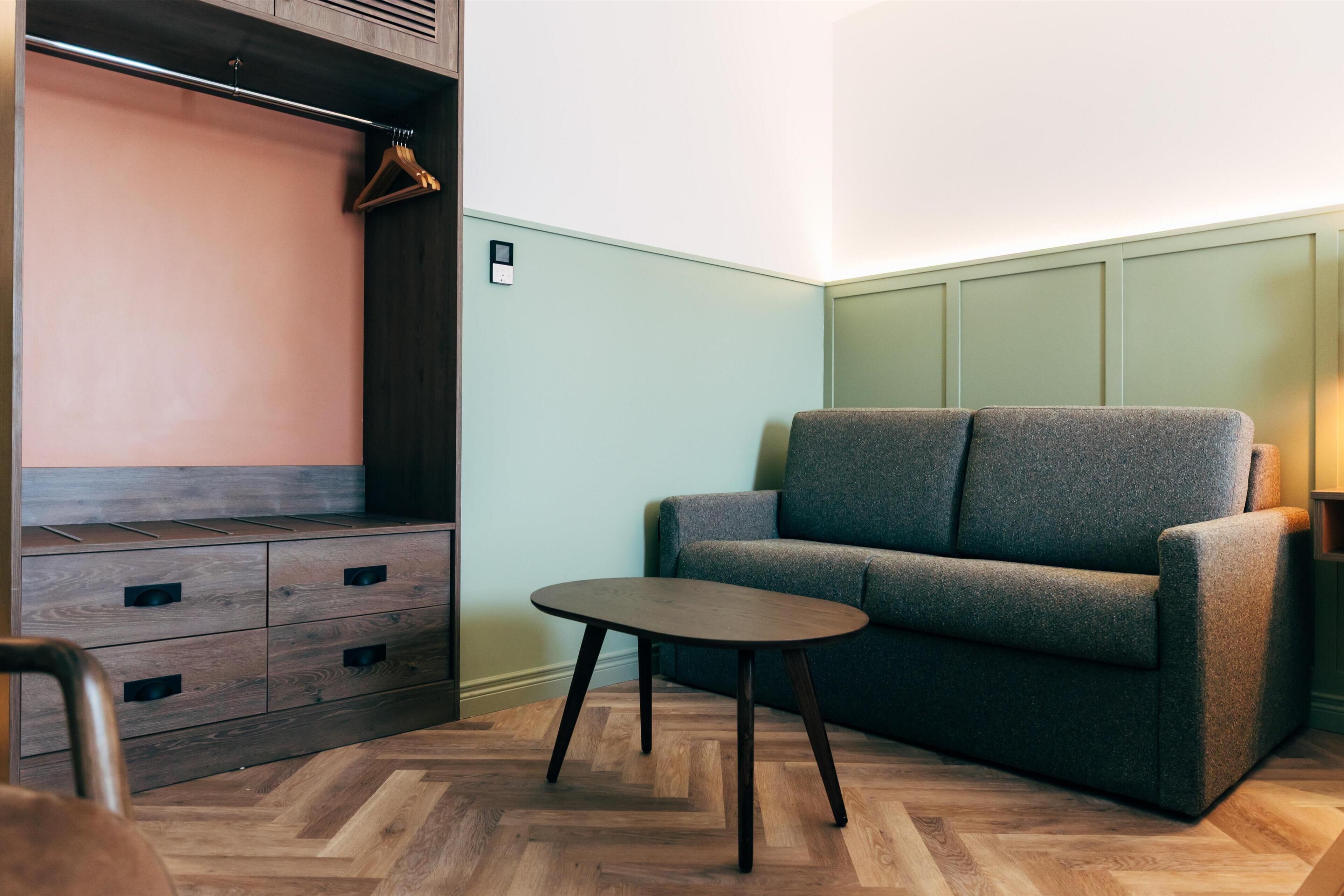 A room with a wooden dresser, a grey sofa, and a small round table.