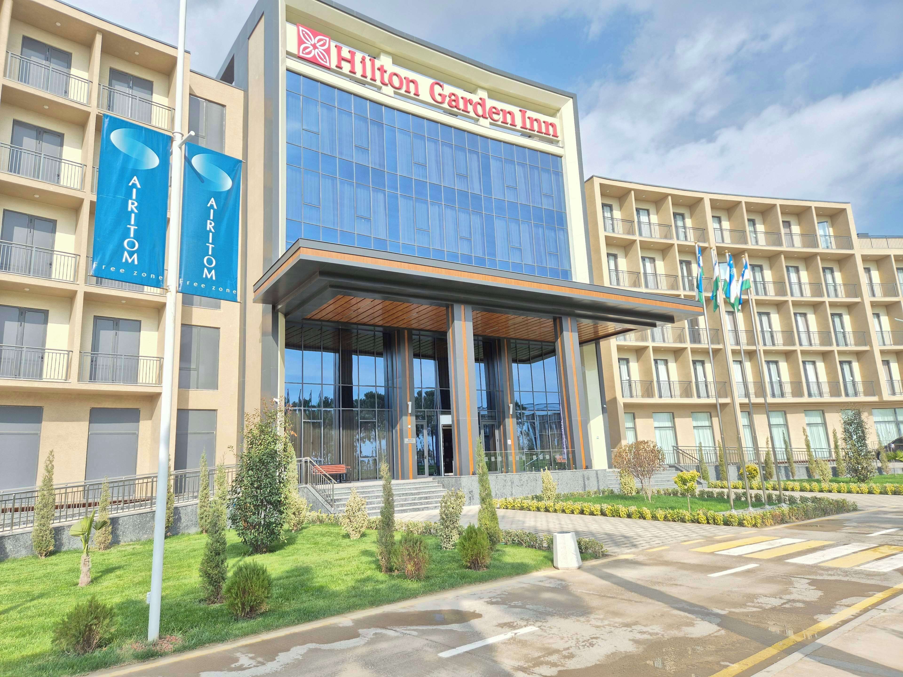A Hilton Garden Inn hotel with a modern facade, large windows, and a well-maintained garden area in front.