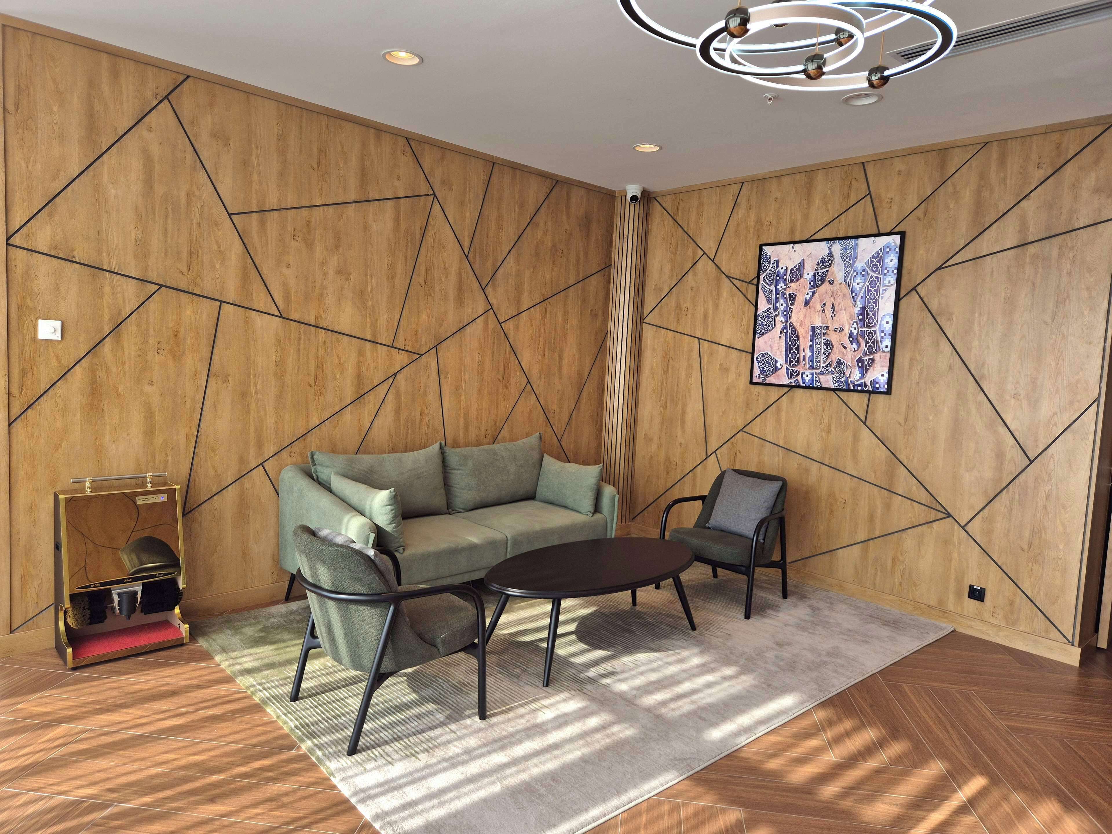 A modern living room with a wooden wall design, a sofa, two armchairs, a coffee table, and a rug.