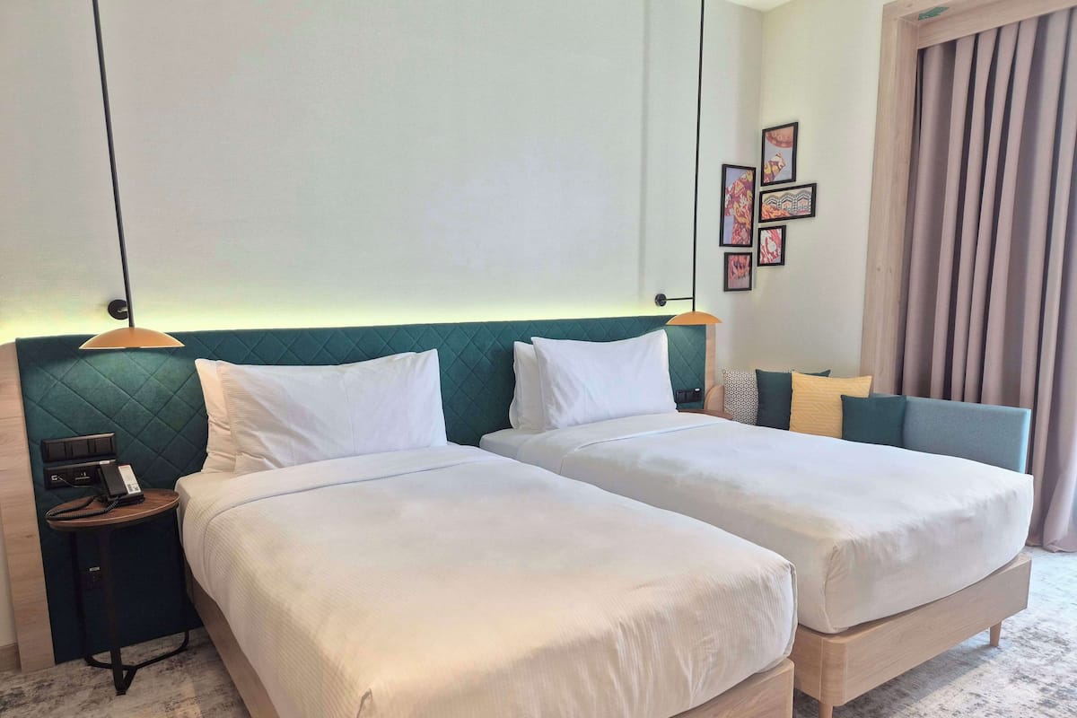 Une chambre d’hôtel avec deux lits simples, une table de chevet avec un téléphone et une lampe fixée au mur.