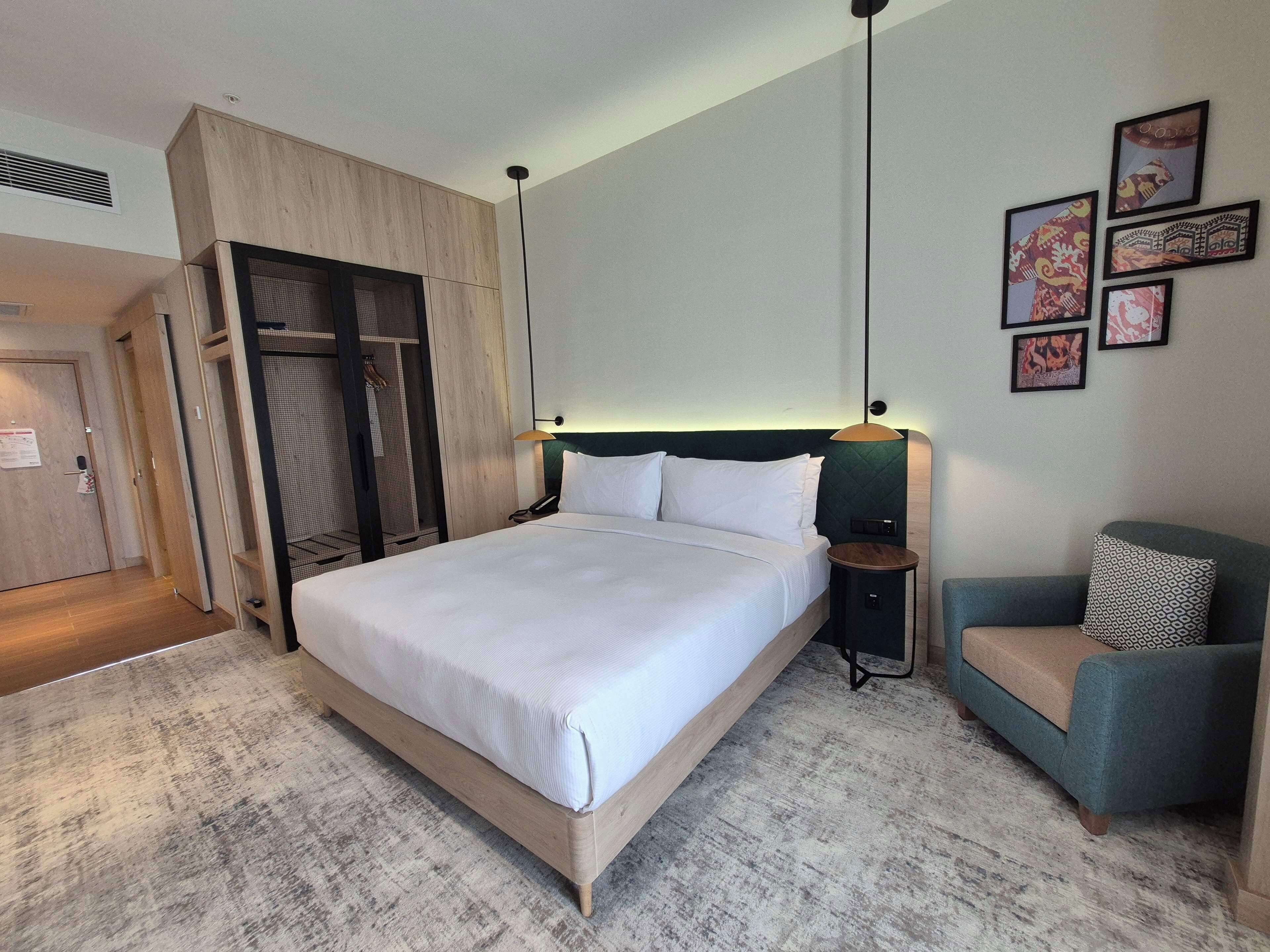 A hotel room with a large bed, a wardrobe, a seating area, and artwork on the wall.