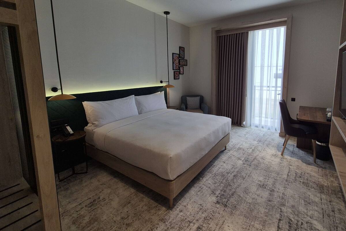 Une chambre d’hôtel avec un grand lit, un bureau, une chaise, une table de chevet et une fenêtre avec des rideaux.