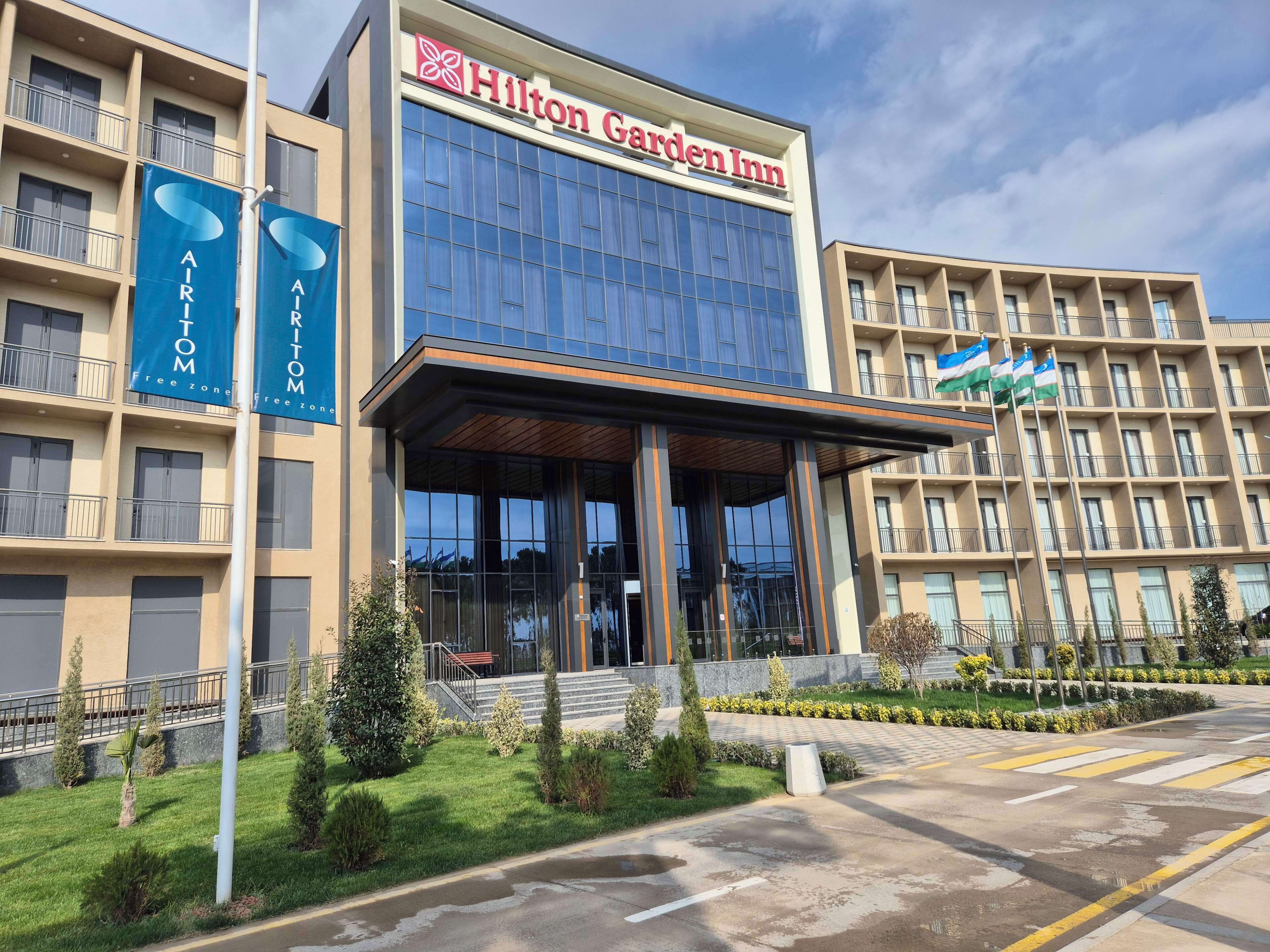 Un hotel Hilton Garden Inn con fachada moderna, amplios ventanales y césped cuidado.