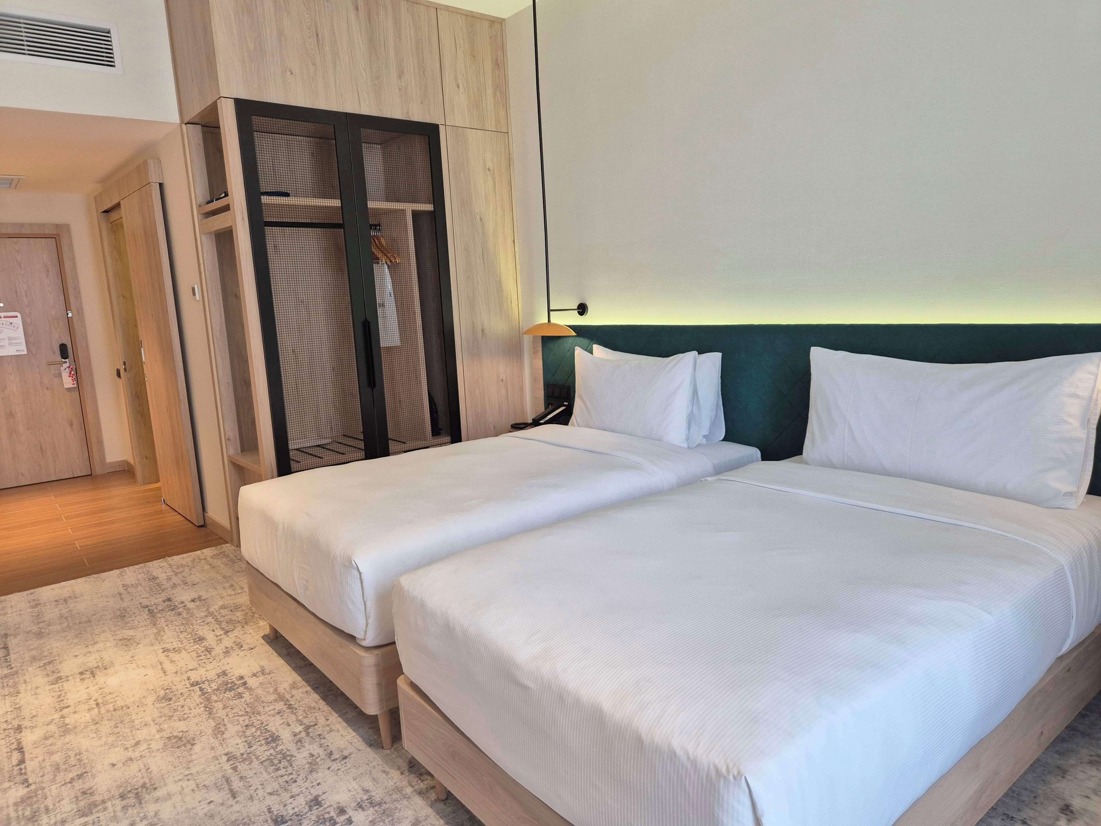 A hotel room with two beds, a wooden wardrobe, and a green headboard.