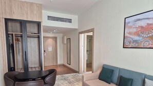 Una camera d'albergo moderna con un divano, un tavolo da pranzo e sedie. Si vede un bagno con doccia attraverso una porta aperta.