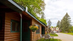 A log cabin with a porch, outdoor seating, and a hanging flower basket. - Cozy 2BR 1BA Cabin #6 Riverside Point Resort (Park Rapids)