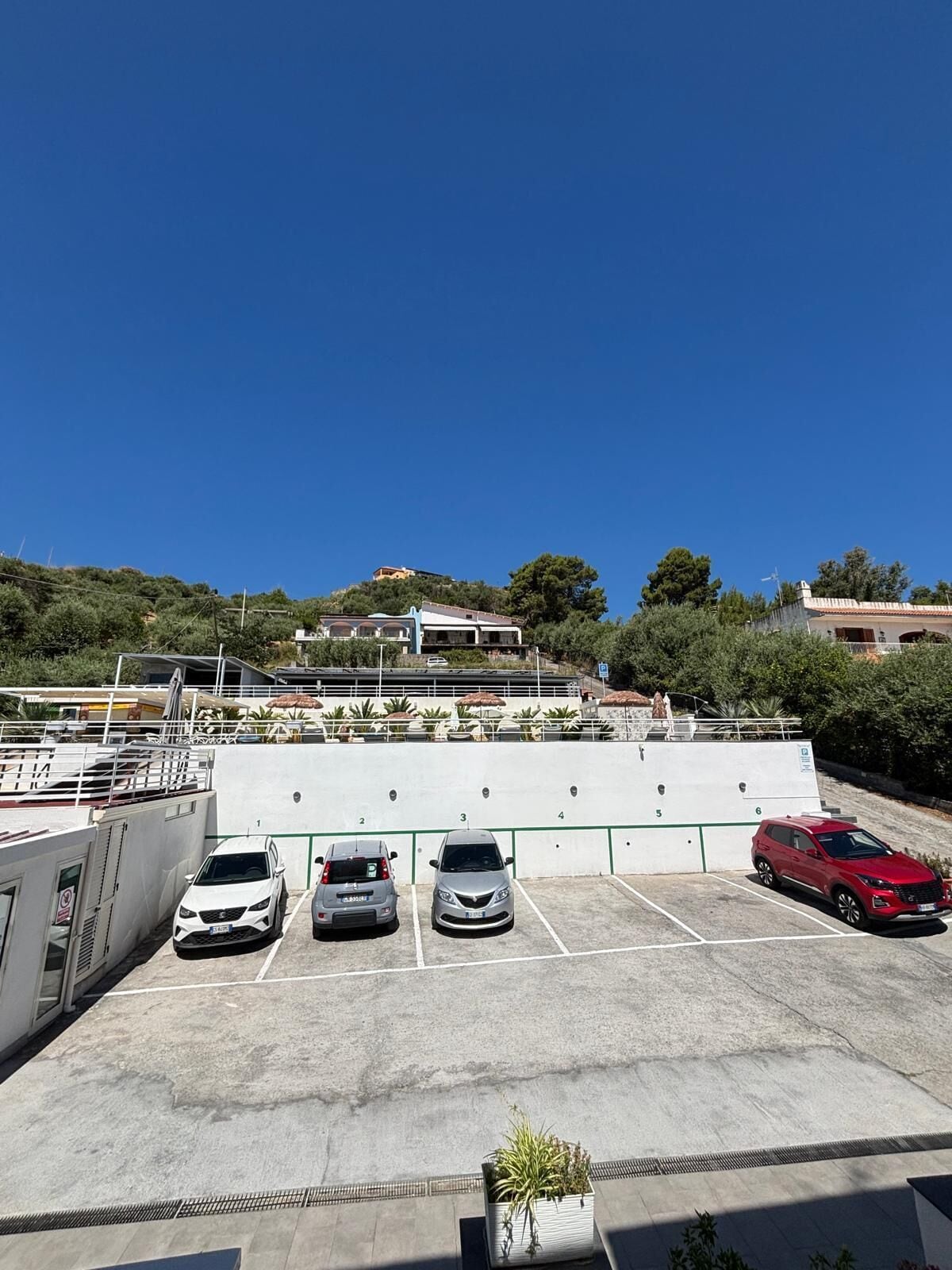 A parking area with six marked spaces, a white building with a red roof, and a clear blue sky.