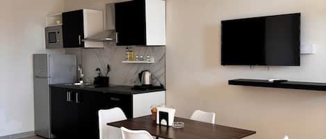 A modern kitchen with a dining area, featuring a flat-screen TV, a microwave, a refrigerator, and a coffee machine.